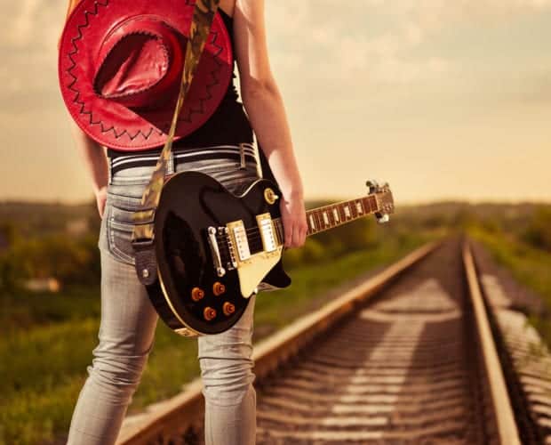 Girl standing in railway with red cowboy hat and black guitar