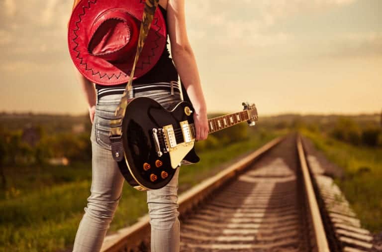 Girl standing in railway with red cowboy hat and black guitar