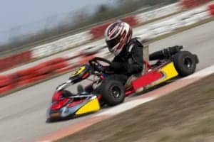 A young driver in a helment riding downhill in a go kart.
