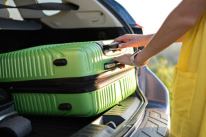 woman putting a green suitcase in the back of a car
